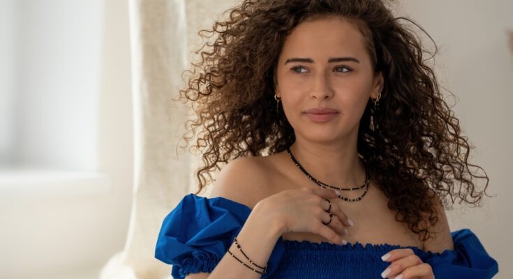 Kobieta w biżuterii MOON LOVE – naszyjnik, bransoletka i pierścionek z czarnymi kamieniami i złotymi elementami. Elegancka stylizacja z niebieską sukienką.